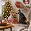 Wicked Glinda and Elphaba Christmas ornament features the two characters holding hands, held against a bokeh holiday tree.