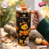 Hand holding a 40oz Stanley tumbler with Winnie the Pooh Halloween pumpkin graphics and a black witch hat.