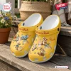 Pair of yellow clogs featuring cartoon character prints and decorative charms on a wooden surface.