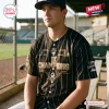 Man wearing the WPBL Los Angeles Queens 2026 Champions Black Baseball Jersey while sitting in a dugout.