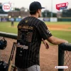 Rear view of a man wearing a WPBL Los Angeles Queens 2026 Champions black baseball jersey at a ballpark.