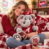 A woman holding a gray Alabama Crimson Tide plush elephant toy wearing a red sweater and beanie while sitting on a couch.