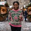 Front view of a woman wearing an Alpha Kappa Alpha 1908 Ugly Christmas Sweater at an outdoor holiday market.