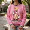 Front view of an Alpha Kappa Alpha pink bear sweatshirt featuring a teddy bear graphic holding an AKA tote bag.