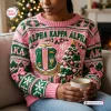 Front view of an Alpha Kappa Alpha pink ugly Christmas sweater featuring green text, a crest, and a holiday tree.