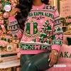 Front view of an Alpha Kappa Alpha pink ugly Christmas sweater featuring green graphics and holiday patterns.