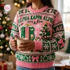 Front view of person wearing Alpha Kappa Alpha pink ugly Christmas sweater holding mug.