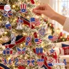 Close-up view of a hand hanging an American flag ornament on a decorated Christmas tree with various patriotic ornaments.