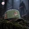 Front view of an Anaheim Ducks x Jason Voorhees olive green baseball cap sitting on mossy wood in a foggy forest.