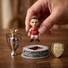 Closeup of a hand holding a miniature Arsenal FC player figurine near a stadium model.