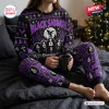 Front view of a person wearing a Black Sabbath Christmas ugly sweater and pants set while holding a mug on a bed.