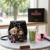 Two plush keychains attached to a black quilted backpack on a marble table.