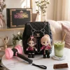 Front view of two plush keychains attached to a black quilted bag alongside a lightstick and drink.