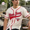 Front view of a cream baseball jersey with red trim and Bon Jovi text worn by a man sitting on a wooden bench outdoors.