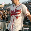 Man wearing a cream baseball jersey with red piping, a winged heart emblem, and red script lettering.