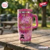 Front view of a pink tie-dye Breast Cancer 41st Anniversary handle tumbler with ribbon graphics on a wooden picnic table.