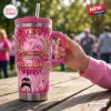 Hand holding a pink Breast Cancer 41st Anniversary 1985-2026 Handle Tumbler on a wooden table outdoors.