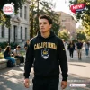 Man wearing a California Golden Bears black hoodie with skull graphic on a college campus pathway.