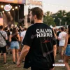 Rear view of a man wearing a black Calvin Harris North America 2027 baseball jersey at an outdoor concert.