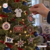 Hand hanging a round logo ornament on a Christmas tree with Chicago Cubs Baseball Christmas Advent Calendar items.
