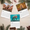 Flat lay of three Danny DeVito wall calendar pages for July, August, and September surrounded by pine branches.