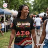 Woman wearing a Delta Sigma Theta Black History Month shirt featuring Juneteenth graphics and a raised fist at an outdoor event.