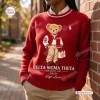 Front view of a red sweatshirt with a teddy bear graphic wearing a varsity jacket and holding a bag.