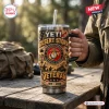 Hand holding Desert Storm Marine Corps YETI Tumbler Cup on outdoor wooden table.
