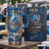 Front view of Detroit Lions 96th Anniversary Tumbler with Handle next to matching box on a wooden table.
