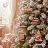 Close-up view of a frosted Christmas tree hanging five miniature ornaments including a pink train and guitar player.