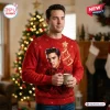 Front view of a man holding a mug while wearing a red Elvis Presley Ugly Christmas Sweater near a lighted tree.