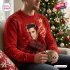 Front view of a man wearing a red Elvis Presley Ugly Christmas Sweater while holding a mug near a tree.