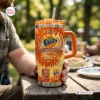 Close-up of a person holding an orange Fanta 86th Anniversary YETI Handle Tumbler outdoors.