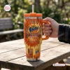 Hand holding orange Fanta 86th Anniversary YETI Handle Tumbler on wooden table.
