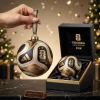 Hand holding a gold and black Trionda Ball Christmas Ornament next to its matching presentation box.