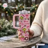 Person holding a pink Grinch Christmas 40oz tumbler with holiday graphics on a wooden table outdoors.