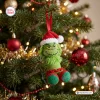 Closeup of a green yarn crochet ornament wearing a red and white Santa hat hanging on a pine tree.