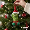 Closeup of a Grinch Crochet Christmas Ornament hanging on a lit pine tree branch.
