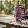 Outdoor view of a red, white, and blue tie-dye Honda 78th Anniversary 1948-2026 Handle Tumbler on a wooden picnic table.