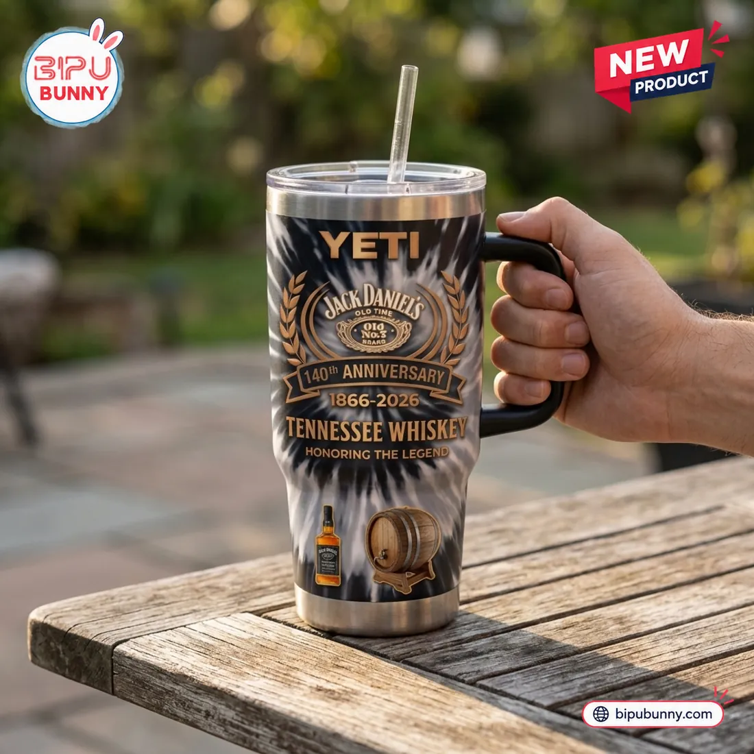 Hand gripping the black side handle of the Jack Daniels 140th Anniversary YETI Handle Tumbler outdoors above a wooden table