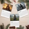 Top view of three 2027 wall calendar pages featuring historical themes on a wooden surface with pine branches.