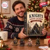 Man holding a Knights Medieval Advent Calendar with four miniature knight figures displayed on the table.