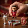 Closeup of a person holding a small figure in a red jersey, with a mini trophy and stadium model.