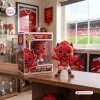 Fred The Red vinyl figure standing next to its box on a wooden desk.