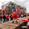 Front view of Manchester United Fred The Red vinyl figure on brick wall outside stadium.