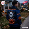 Rear view of a man wearing a blue varsity jacket with horror movie graphics and text on a suburban street.