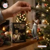 Close-up of hands hanging the Miles Davis 100th Anniversary Resin Ornament on a lit Christmas tree next to its box.