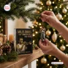 Close-up of hands hanging the Miles Davis 100th Anniversary Resin Ornament on a Christmas tree branch near its gift box.