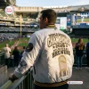 Back view of a man wearing the Milwaukee Brewers 2026 Champions White Bomber Jacket at a stadium.