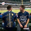 Two fans wearing the Milwaukee Brewers 2026 National League Champions baseball jersey at a stadium.